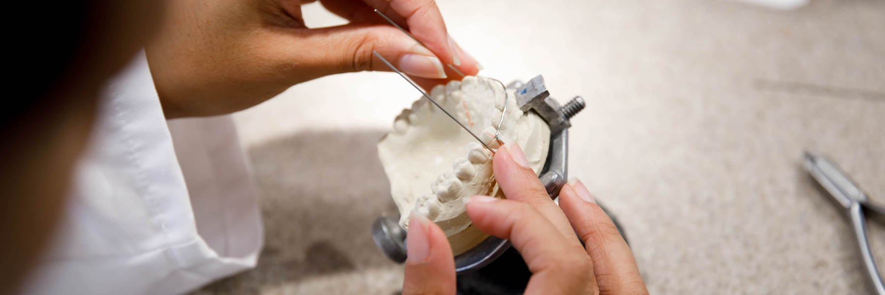 A closeup of a dental lab technician using a plaster mold to shape a wire.